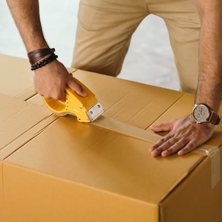 Unrecognizable man sealing box with duck tape while preparing for moving out